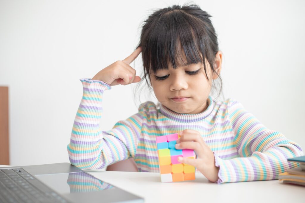 Asian little cute girl holding Rubik's cube in her hands. Rubik's cube is a game
