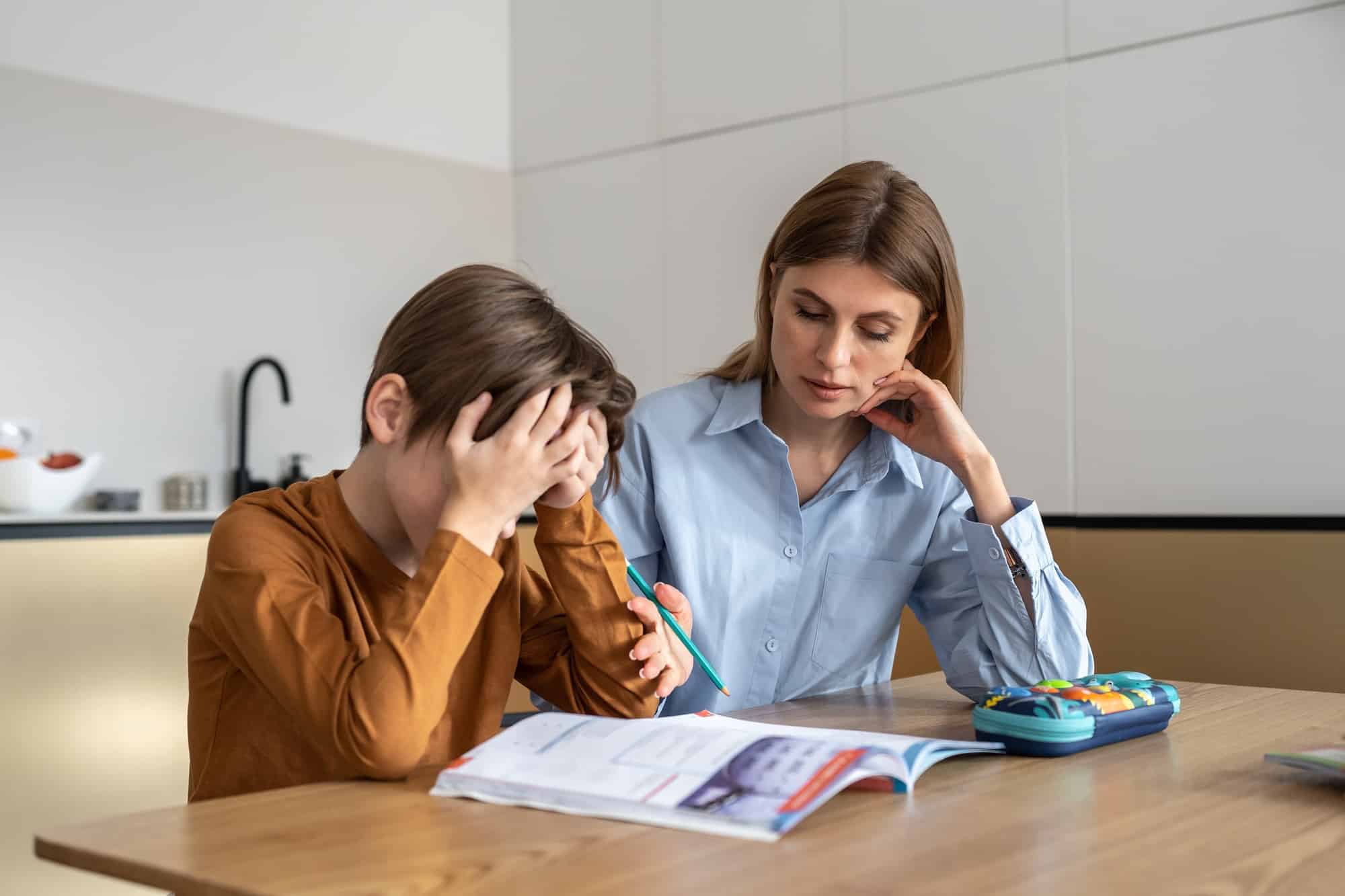 Upset stressed child boy feeling frustrated while doing homework with mom at home